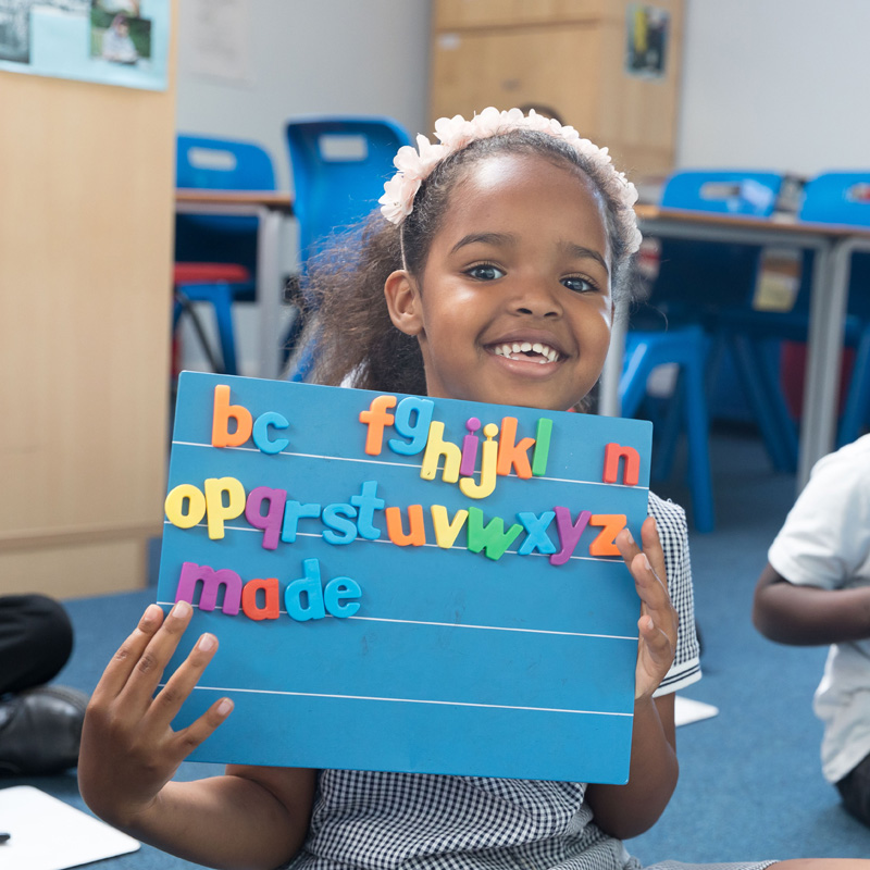 A child holding up a board with letters on.